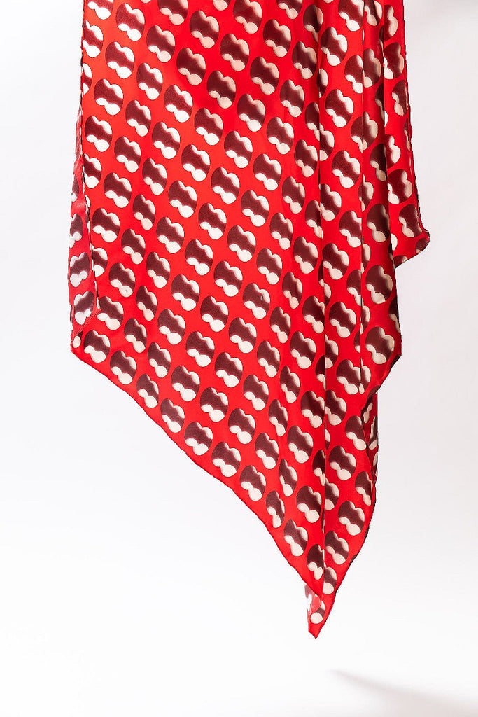 A large silk scarf featuring artwork Double Negative by Cornelia Parker in Red and white is shown suspended with one corner pointing towards the ground