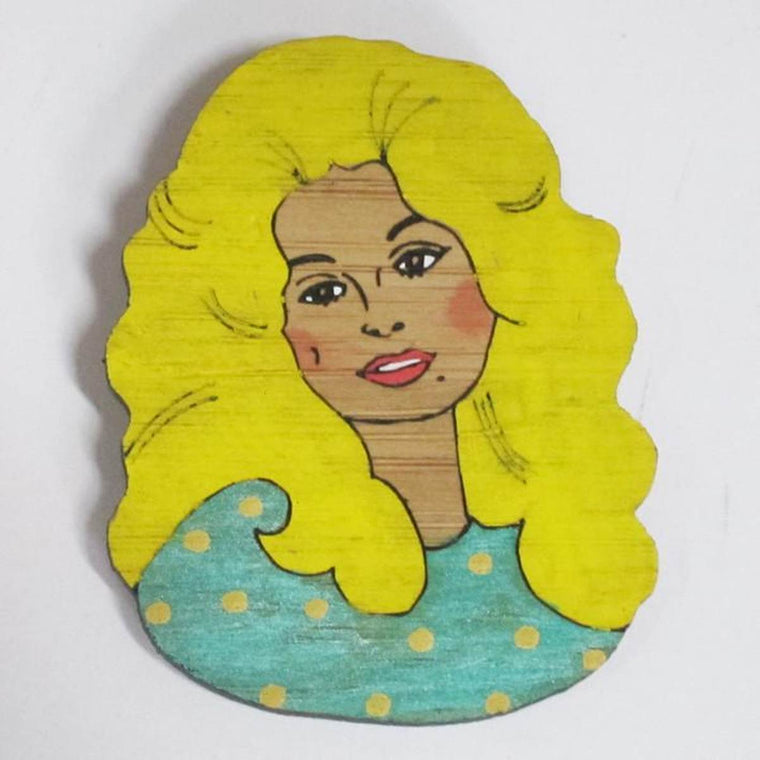 A brooch featuring a portrait of singer songwriter Dolly Parton. She is shown wearing a green top with Yellow polka dots.Made from bamboo wood and hand painted.