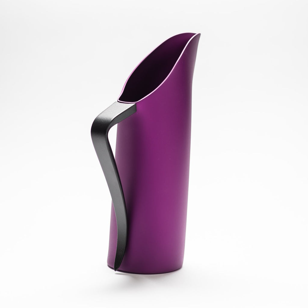 A purple matte jug with its slender black handle facing towards the front, exposing the sculptural opening of the jug.  