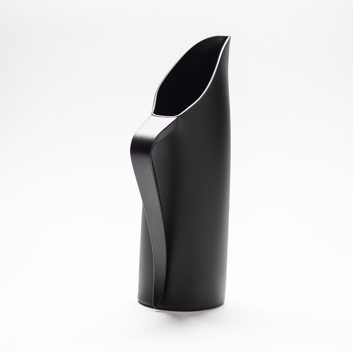A black matte jug with its slender black handle facing towards the front, exposing the sculptural opening of the jug.