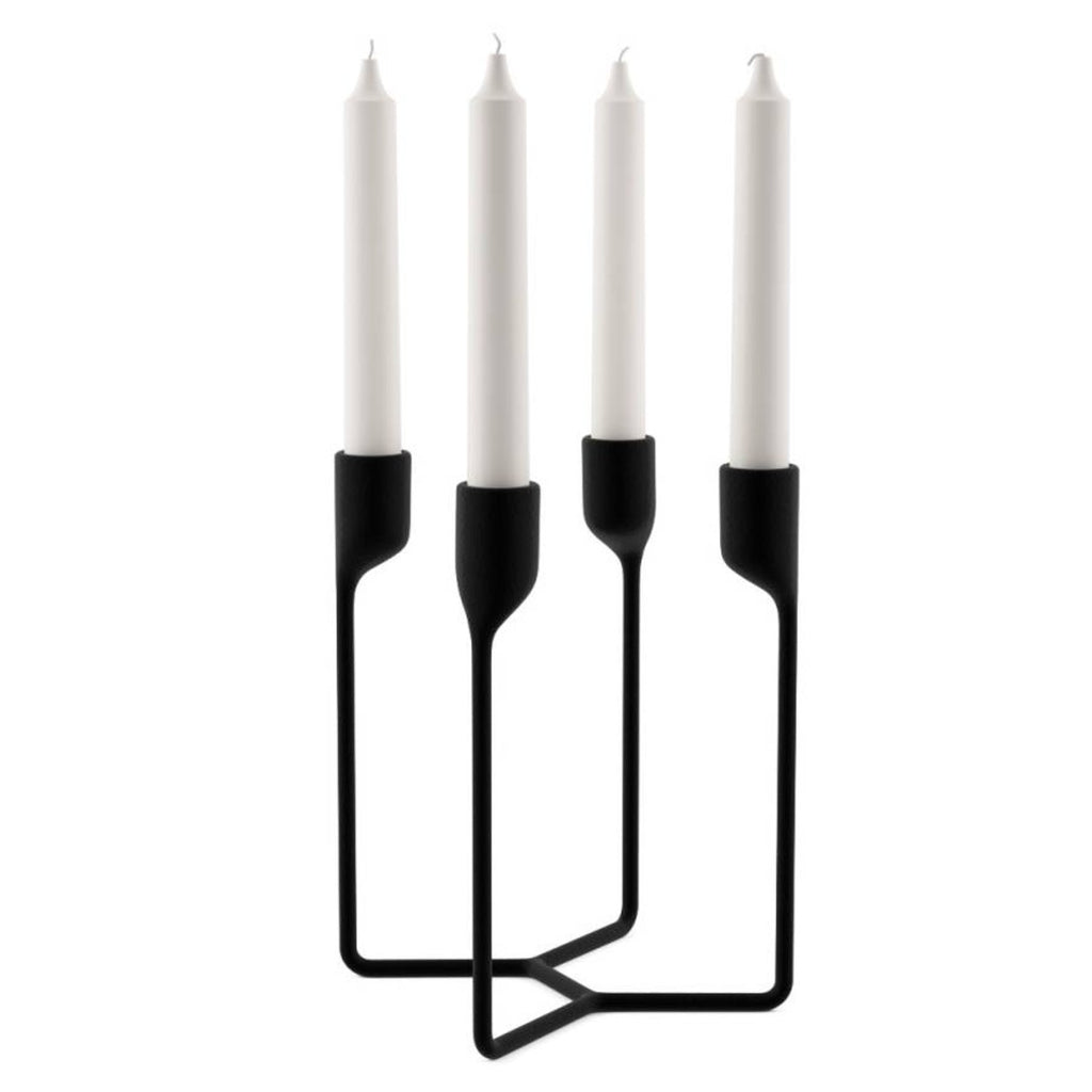 A four-prong candelabra made out of black cast iron holding a white pillar candle in each of its holders.  