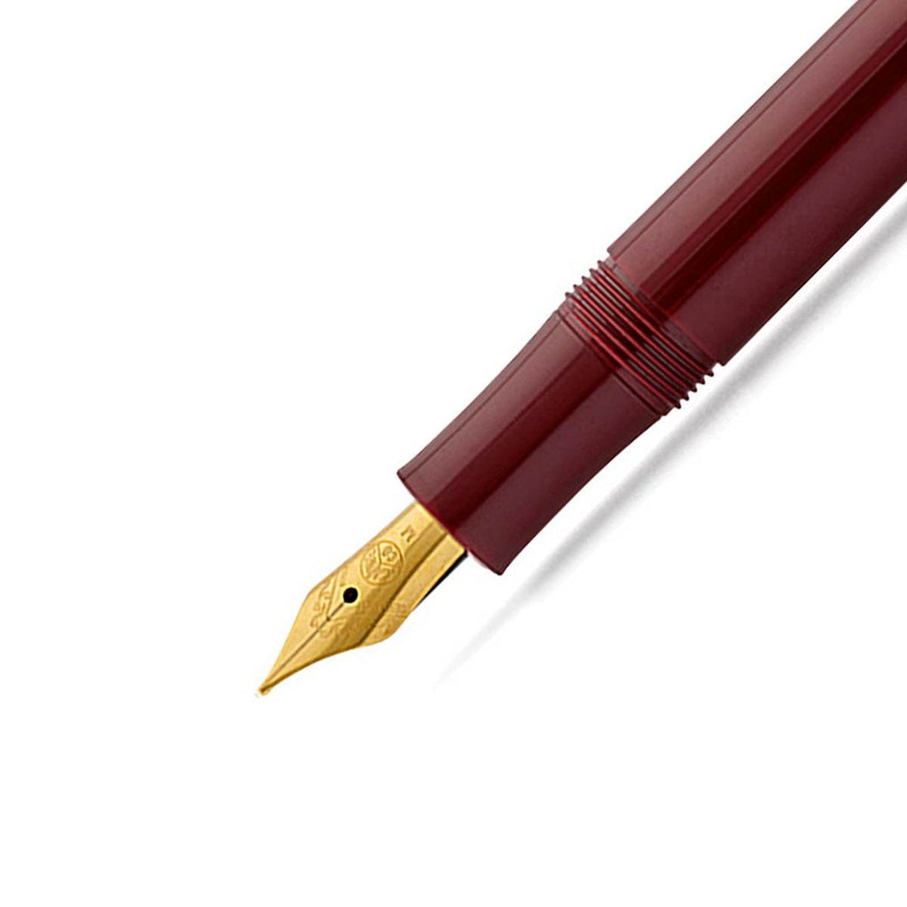 A close up of a fountain gold tip nib on a shiny maroon pen barrel. 
