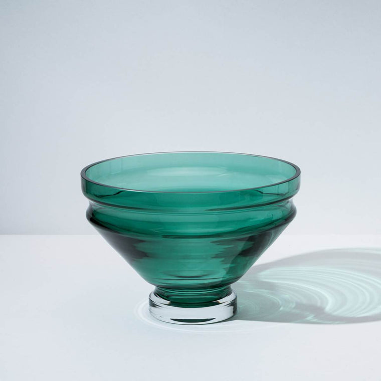 A green glass bowl with grooves at the top, which creates a rippling water effect in the bowl’s shadow