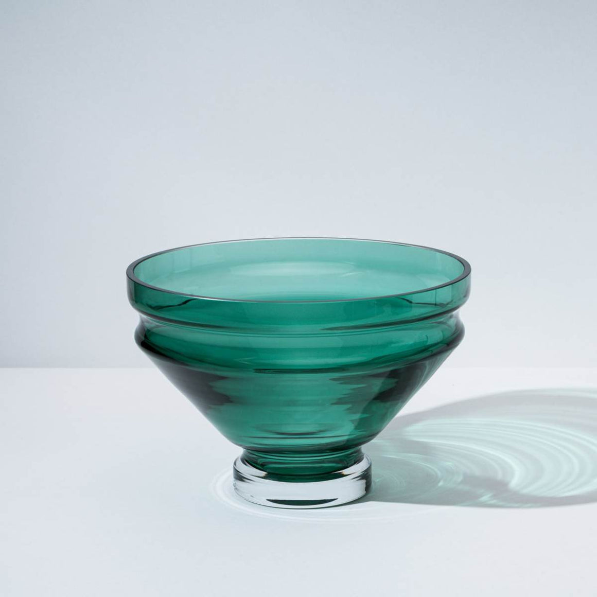 A green glass bowl with grooves at the top, which creates a rippling water effect in the bowl’s shadow