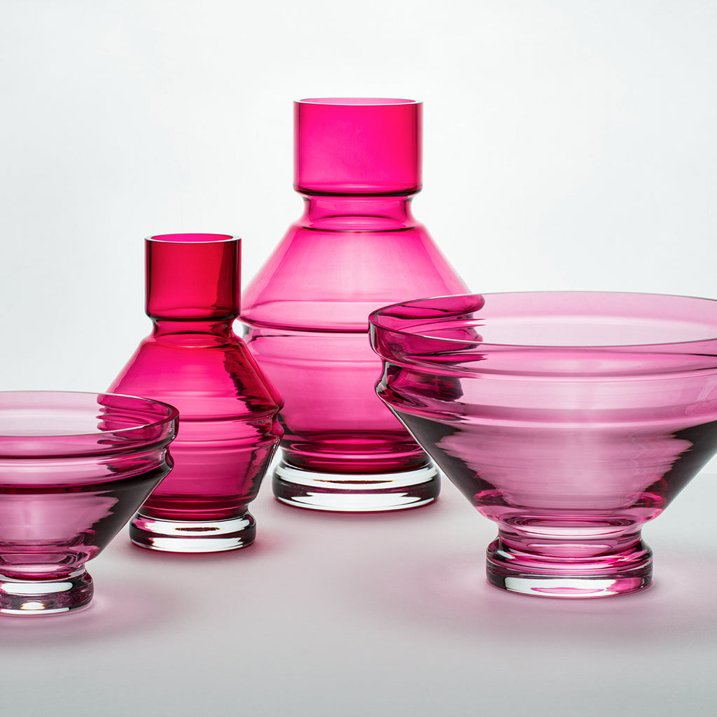 A collection of pink glass vases and bowls, showcasing the refractions that the grooves create.