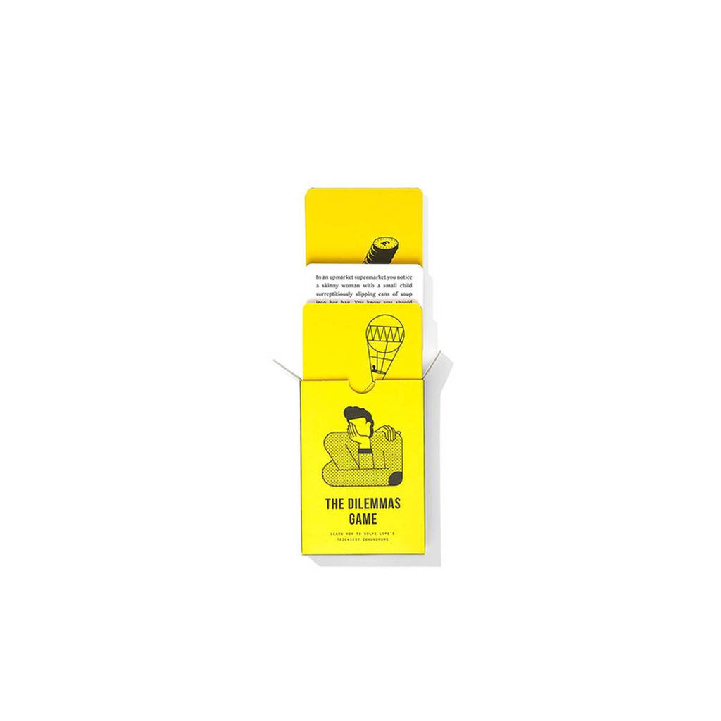 White and yellow cards are sliding out a bright yellow rectangular packaging box with a black graphic of a figure resting its head on its hand and 'the dilemmas game' capitalised in large black font below it. 