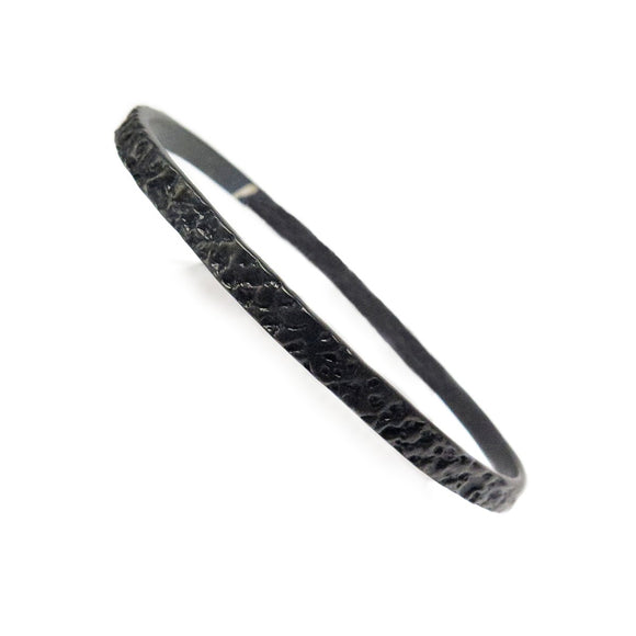 Image featuring a bangle in the center which is black chrome with a gorilla skin imprint