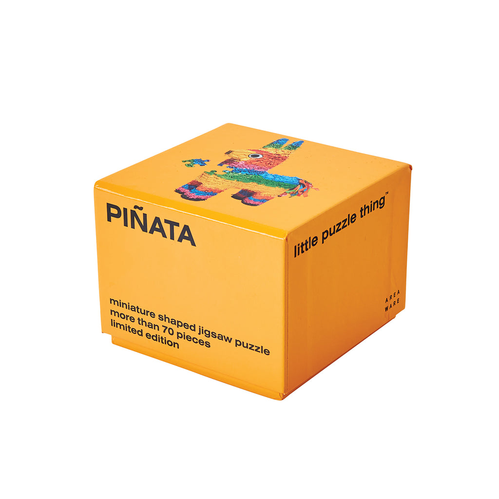 An orange packaging cube has 'pinata' capitalised in black on one side with 'miniature shaped jigsaw puzzle more than 70 pieces limited edition' at the bottom. The top side has an image of the completed pinata puzzle with one piece askew. 