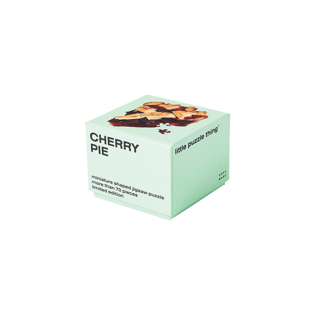 A green packaging cube has 'cherry pie' capitalised in black on one side with 'miniature shaped jigsaw puzzle more than 70 pieces limited edition' at the bottom. The top side has an image of the completed cherry pie puzzle with one piece askew. 
