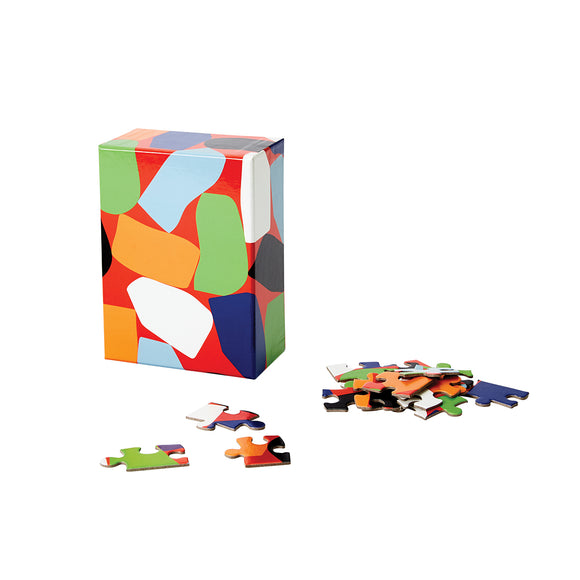 A completed puzzle has a pattern of odd-shaped blocks in green, orange, black, white and blue precariously balanced over a red background. 