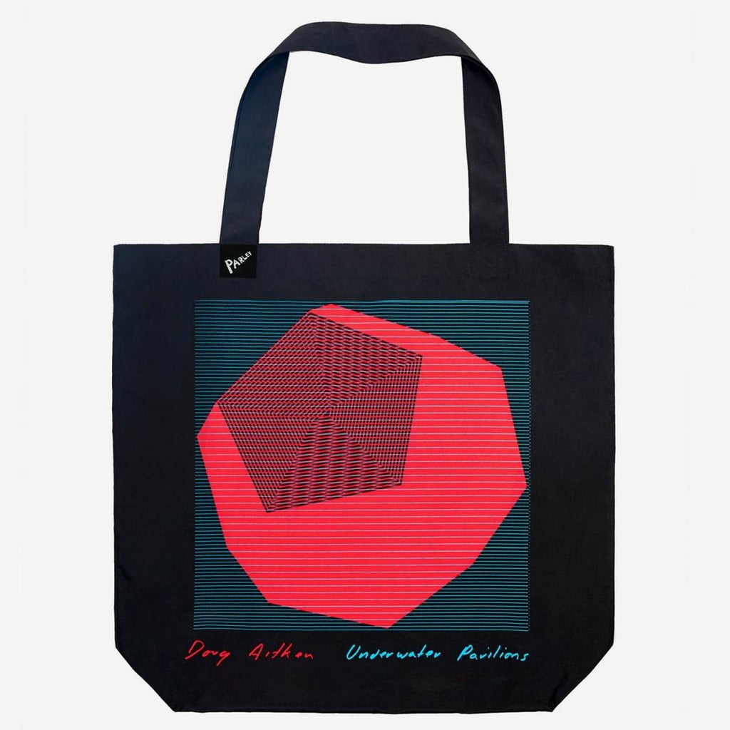 A black tote bag has a graphic design of a 3D red sphere with faceted sides filled with geometric patterned lines inside a blue-lined square. At the bottom of each corner is a handwritten "Doug Aitken" in red on the left and "Underwater Pavilions" in blue on the right.  