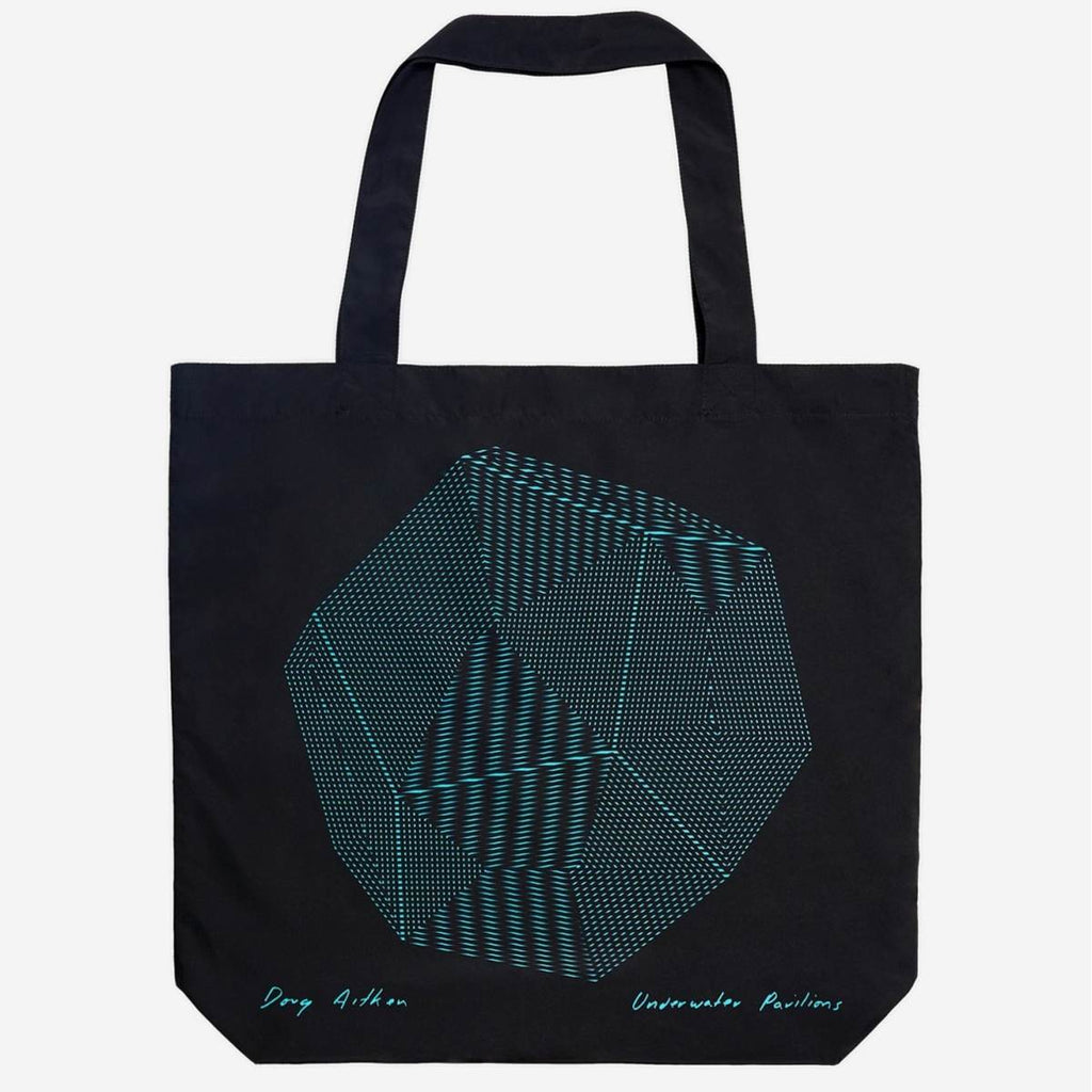 A black tote bag has a graphic design of a 3D blue sphere with faceted sides filled with geometric patterned lines. At the bottom of each corner is a teal handwritten "Doug Aitken" on the left and "Underwater Pavilions". 