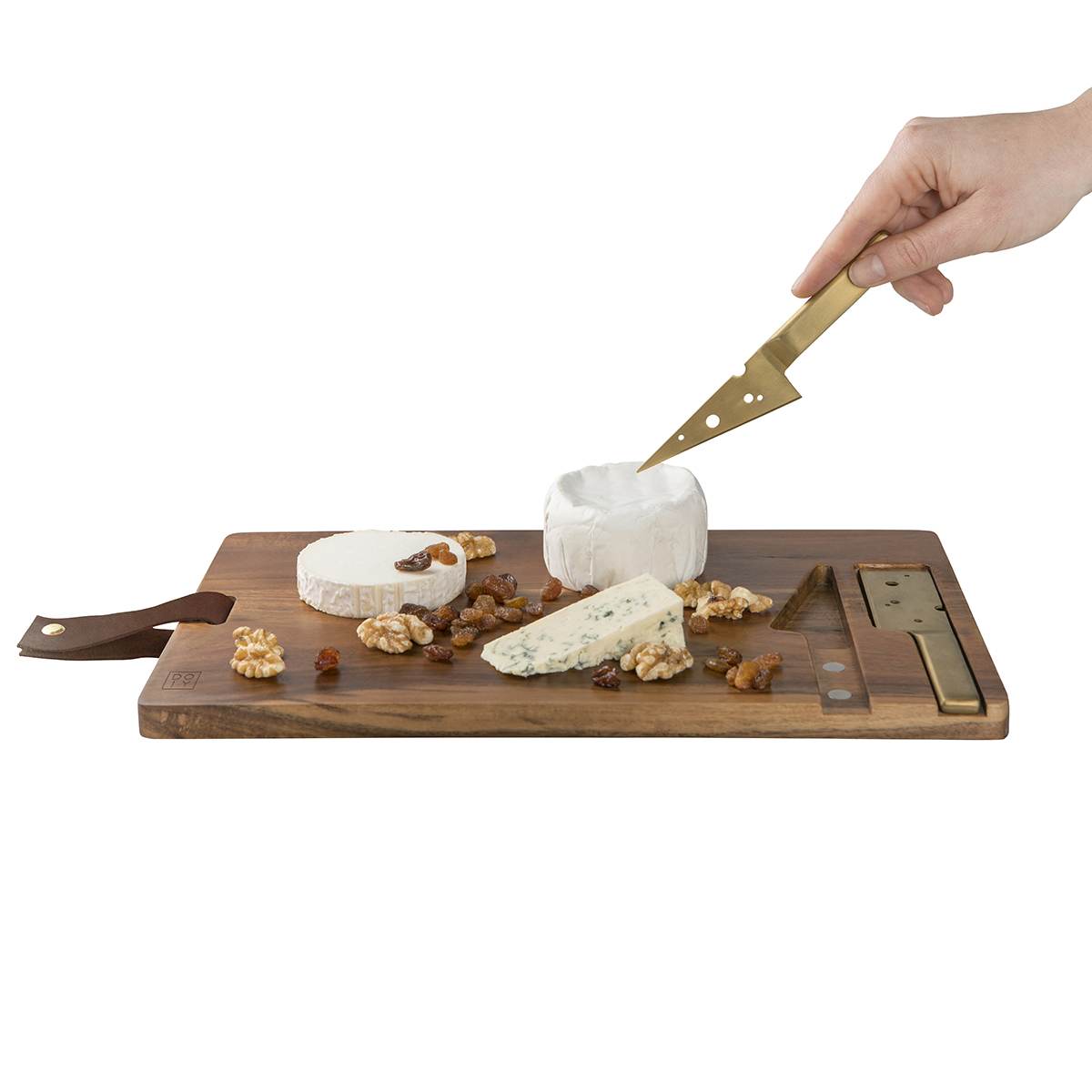 A white round cheese about to be cut by the gold cheese knife on an acacia wood cheese board with walnuts and blue cheese.