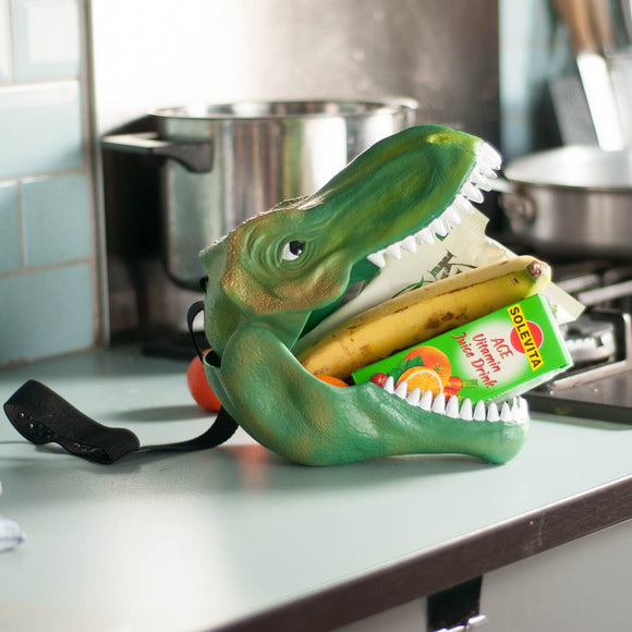 A children's lunch box or storage case in the shape of a Green Tyrannosaurus Rex Head, Shown closed with the carry strap attached, which appears like a harness for the dinosaurs head. Attached tag read " DINO CASE : Keep your goods in safe fangs"