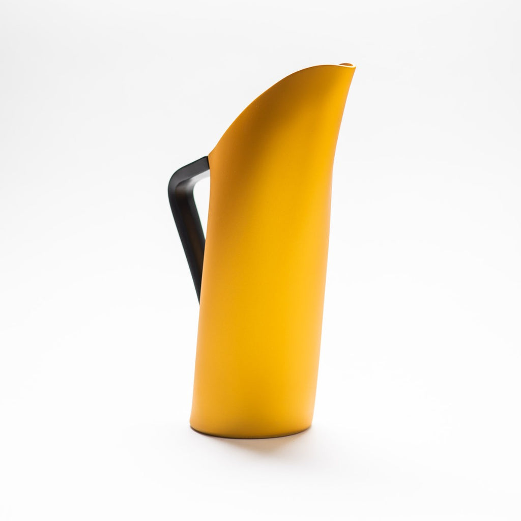 A yellow matte jug with arched spout seamlessly continuing down to its handle. 