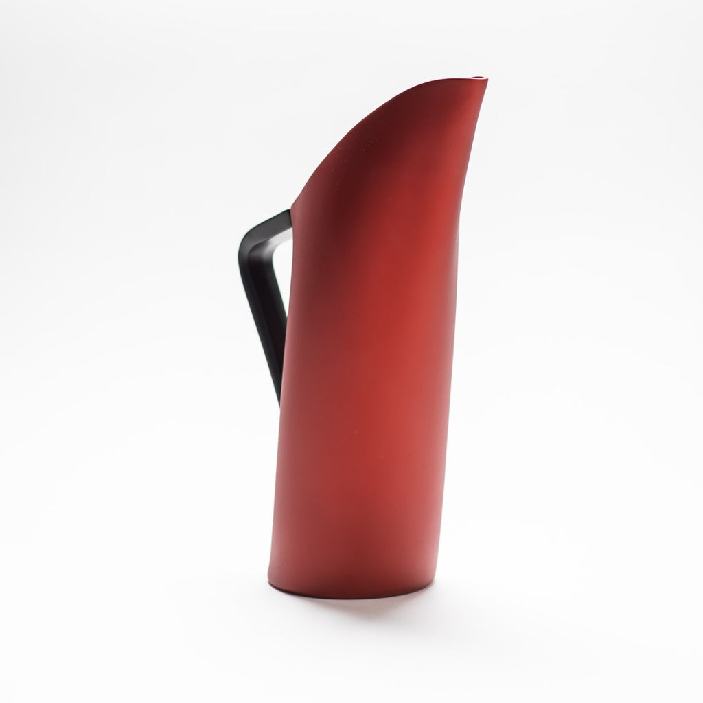 A red matte jug with arched spout seamlessly continuing down to its handle. 