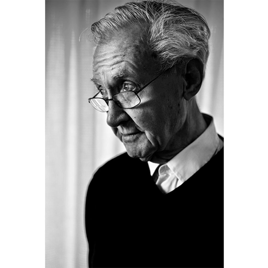 A black and white portrait of Herbert Krenchel gazing to the left with his glasses resting just below the bridges of his nose. Herbert Krenchel has combed white hair and is wearing a white shirt under a black jumper.