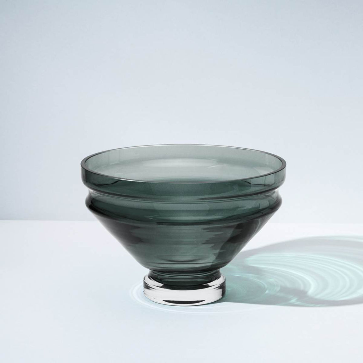 A smoky grey glass bowl with grooves at the top, which creates a rippling water effect in the bowl’s shadow
