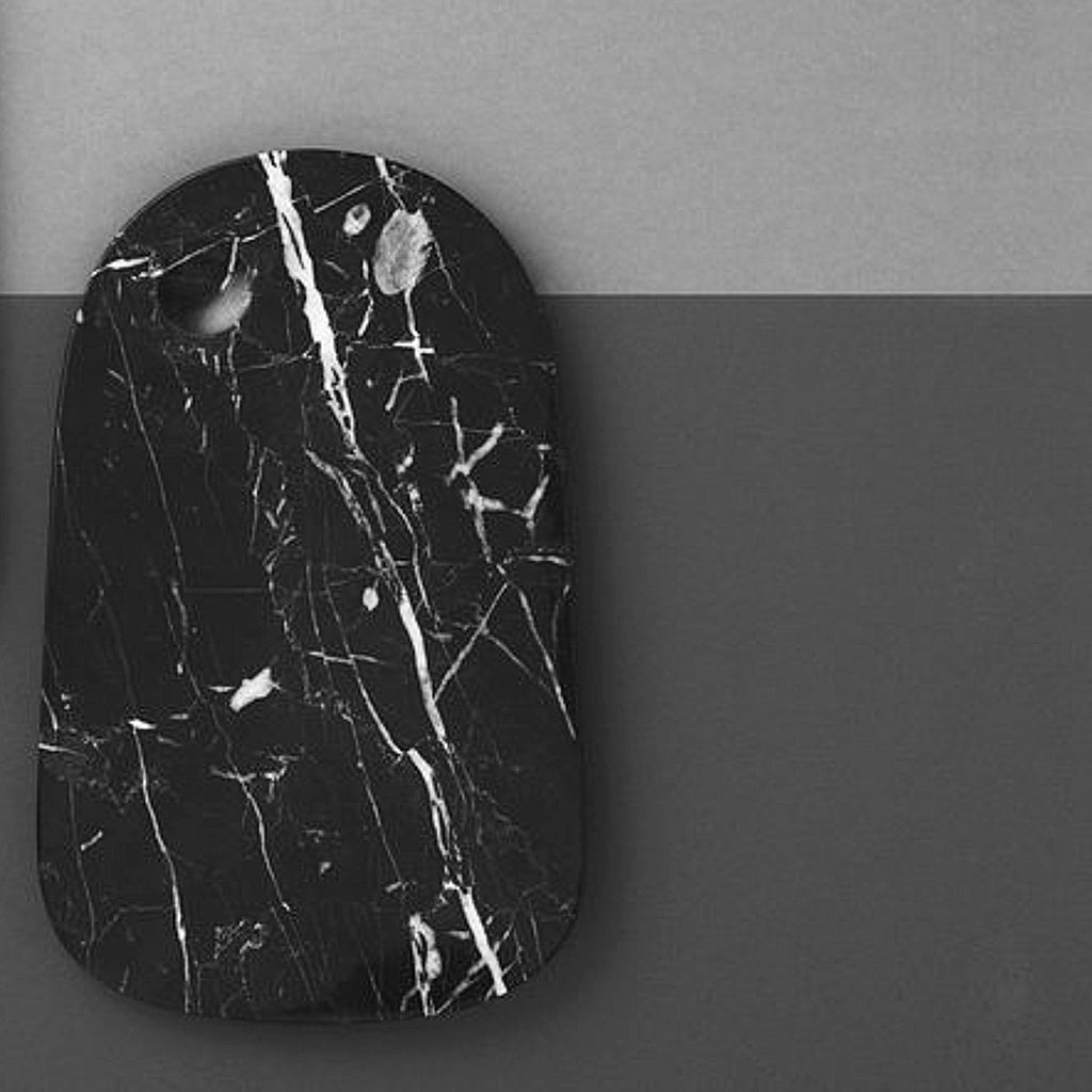 A rectangular serving board with curved corners on one end and the other being rounded is made of black marble with white veins crackle details sits against a grey background.