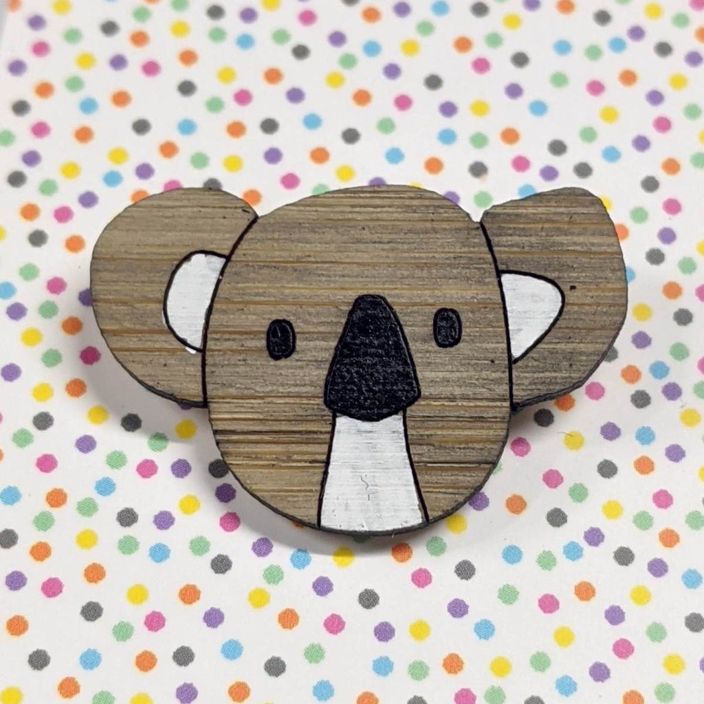 A pin style brooch depicting a koalas head. Made from bamboo wood and hand painted. Shown on a polka dot background.