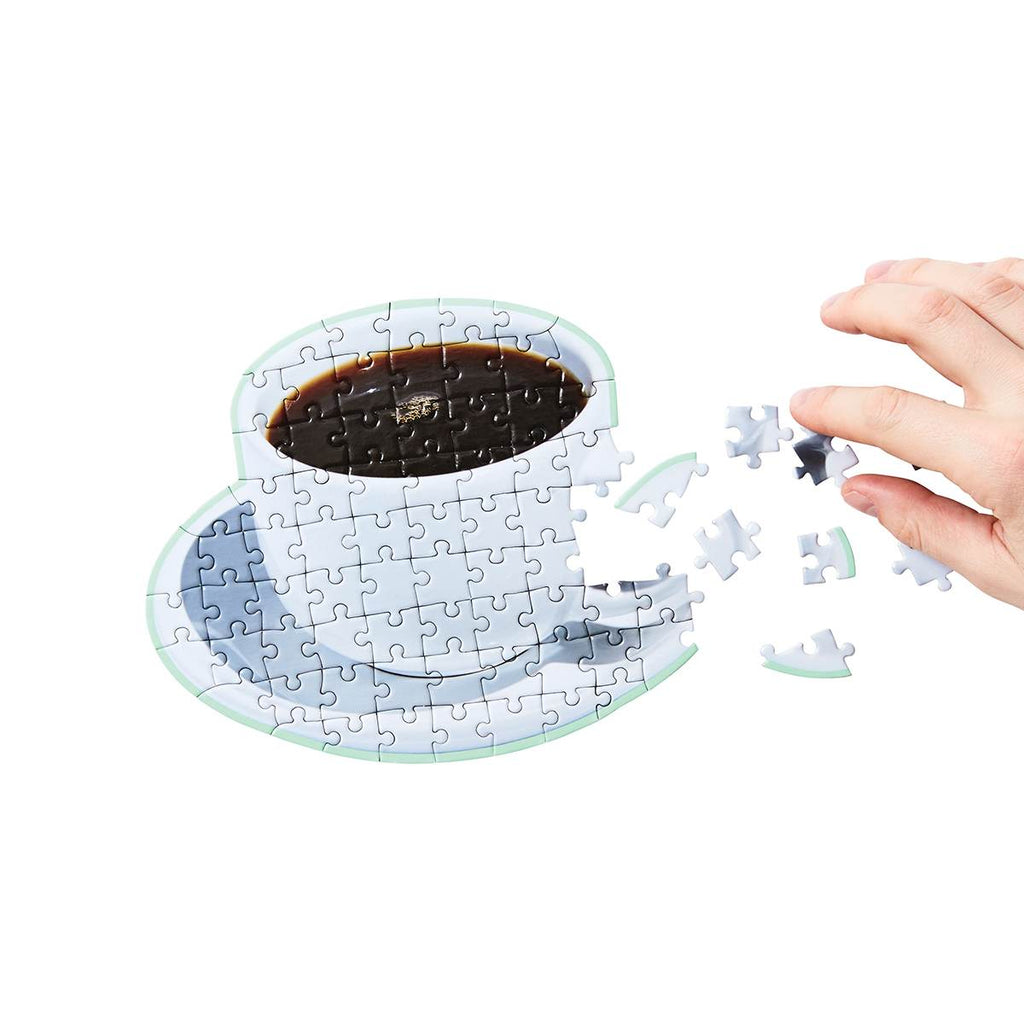 A hand reaching for the scattered side pieces is completing the puzzle in the shape of the photographed coffee in a white cup. 