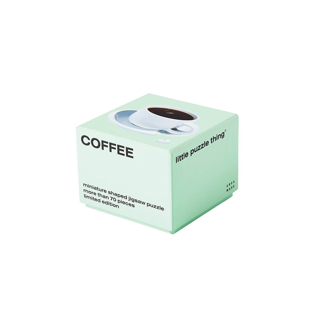 A green packaging cube has 'coffee' capitalised in black on one side with 'miniature shaped jigsaw puzzle more than 70 pieces limited edition' at the bottom. The top side has an image of the completed white cup of coffee puzzle with one piece askew. 