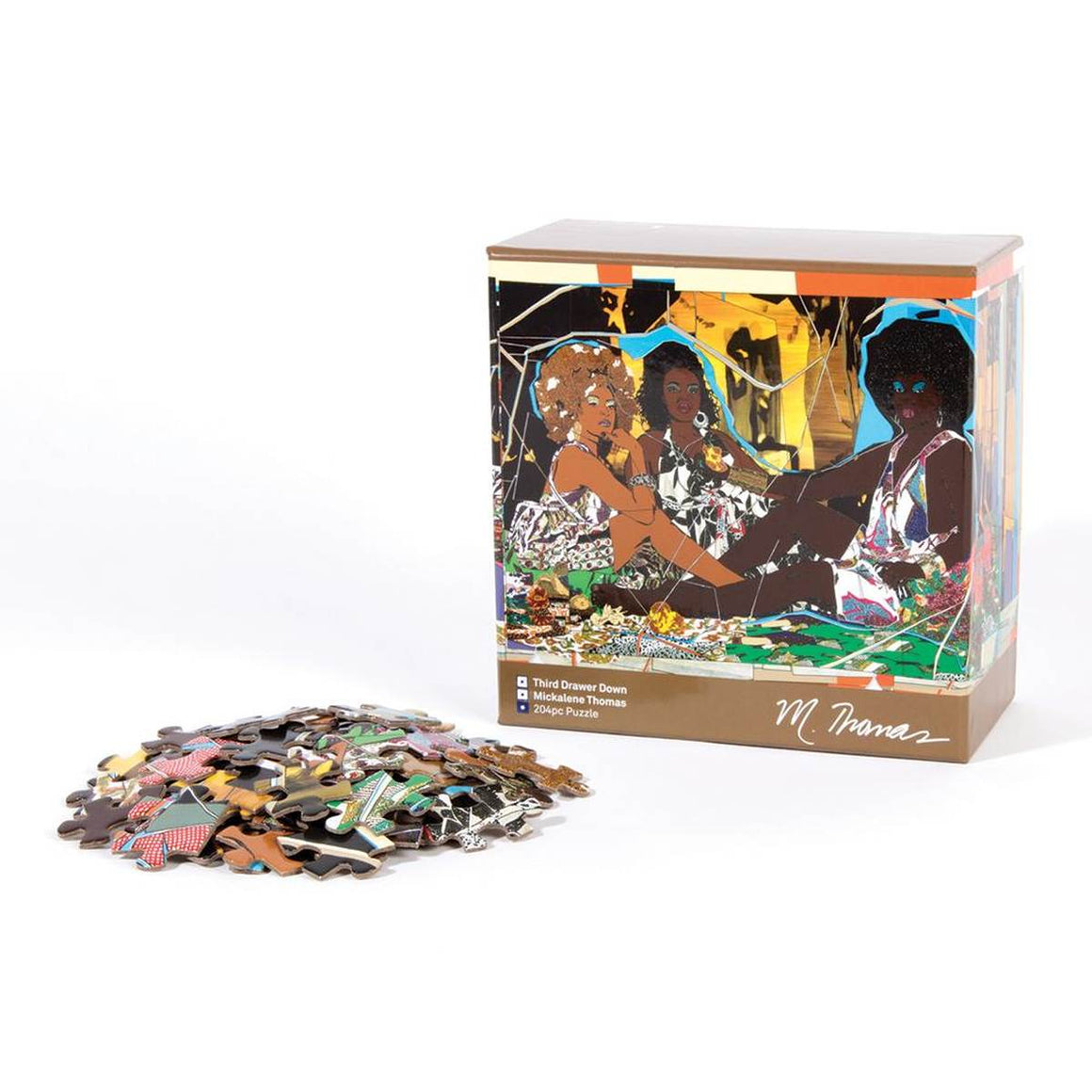 A pile of puzzle pieces is in front of its brown square packaging box with a collaged painting of three brown-skinned women in patterned dresses. 