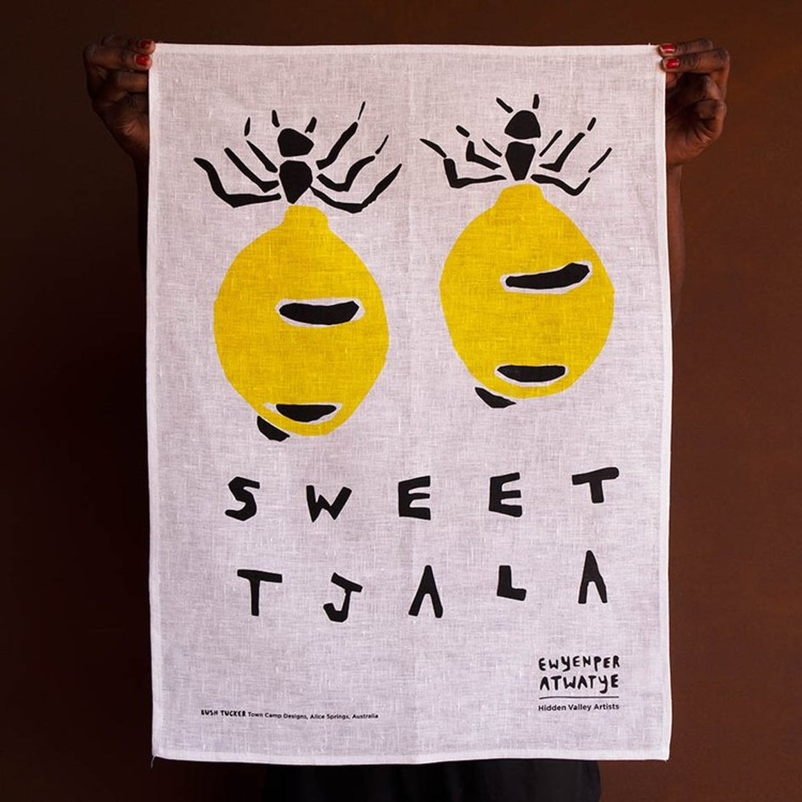 A screenprinted Tea Towel designed by Aboriginal artist Patricia Robinson. Two honey ants are depicted above the text " SWEET TJALA"