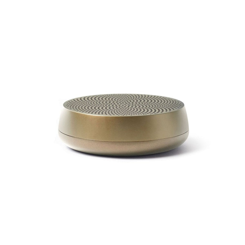 A gold cylindrical speaker with a low profile and a round base. 