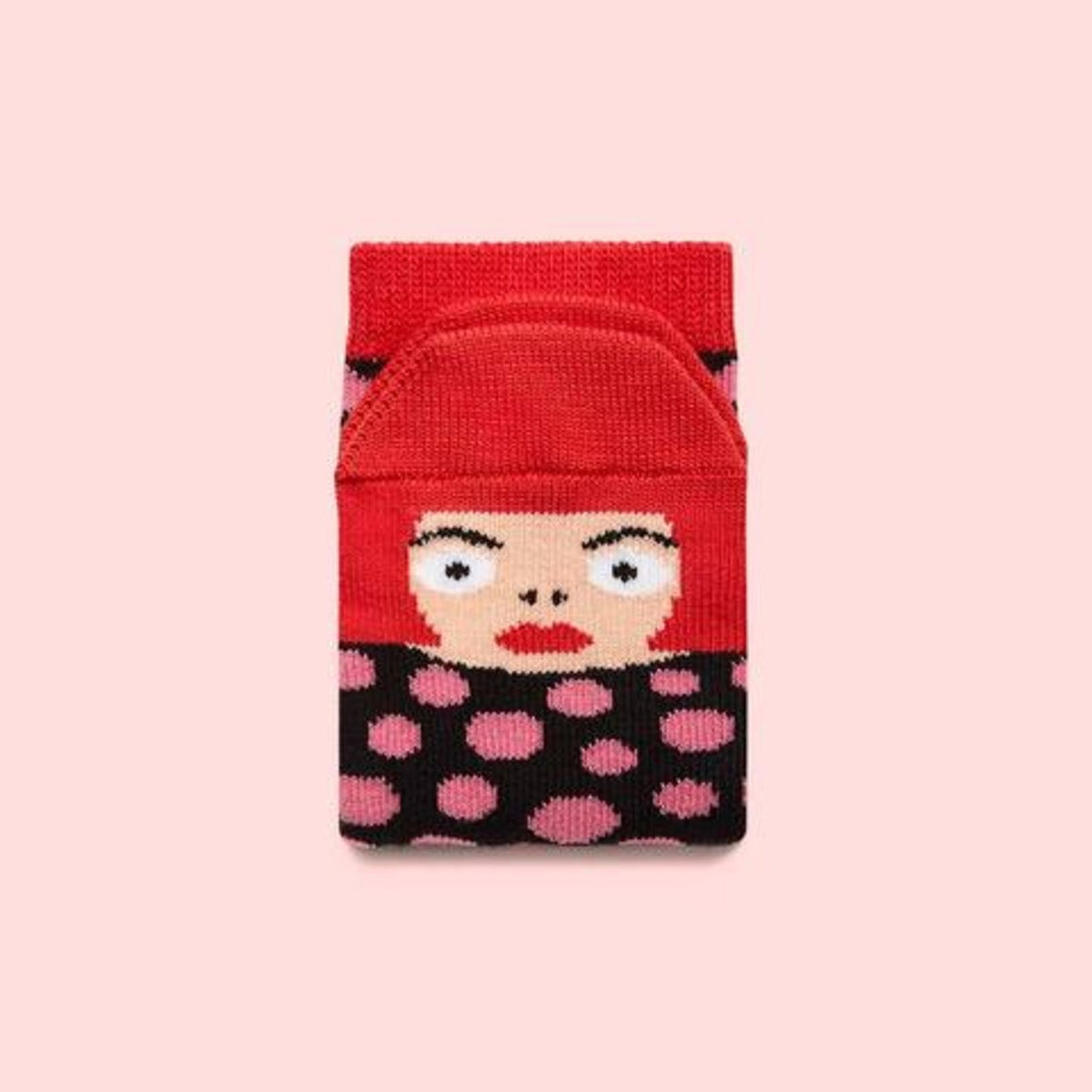 A sock with a cherry red band folded on a blush pink background shows the toe end with Yayoi Kasuma's face and cherry red bob.  