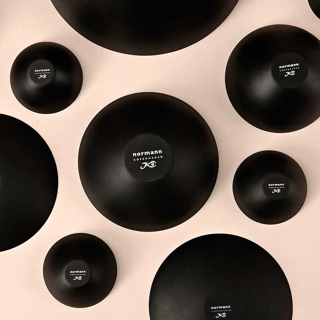 Multiple Krenit bowls sitting upside down, showcasing its logoed bases and black outer surface, creating a polka dot effect in the flat lay shot. 