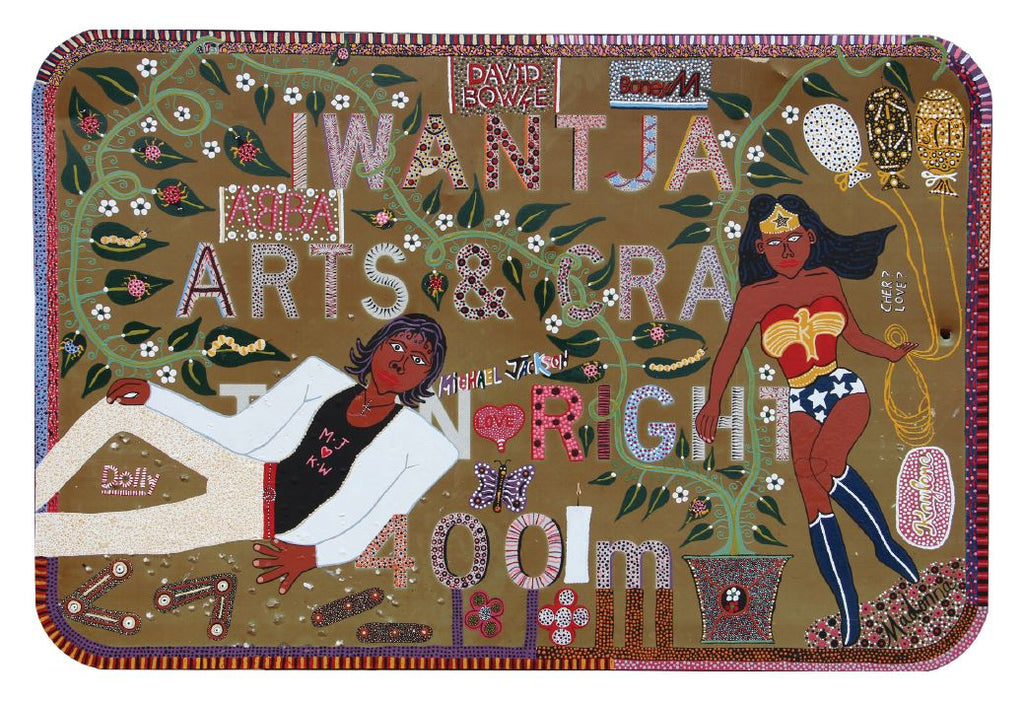 A horizontal postcard with a white border depicts Kaylene Whiskey's Welcome to Iwantja Arts featuring a dark-skinned Wonder Woman holding three balloons with an Indigenous dot pattern and a dark-skinned man lying on the side with a 'MJ love KW' on the black shirt under the white blazer. At the same time, green vines travel from the pot at the bottom. 