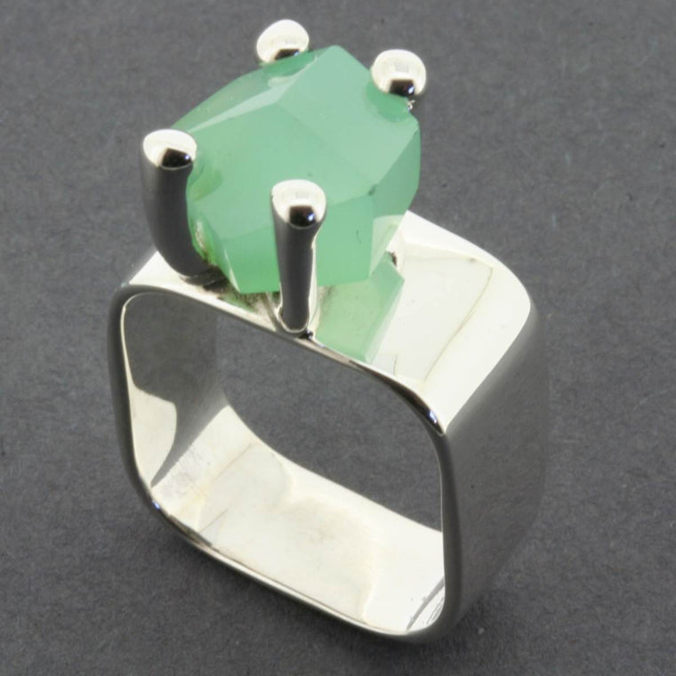 A silver band style ring, featuring a claw set rough cut Chrysoprase stone. The stone is a pastel green and the setting is slightly off centre.