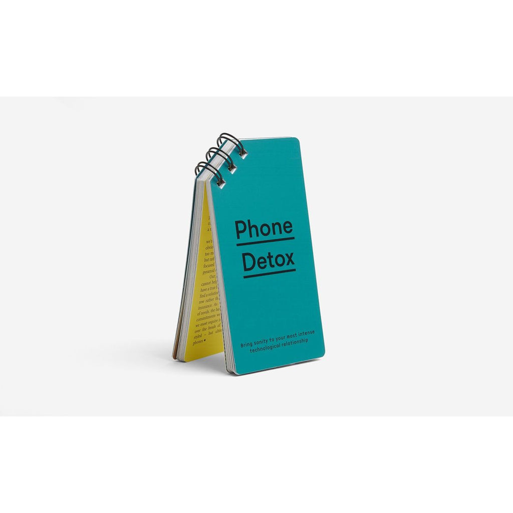 Standing upright on a white background is a notepad with the binder spine on the top left corner and a teal cover with "phone detox" underlined in black font. 