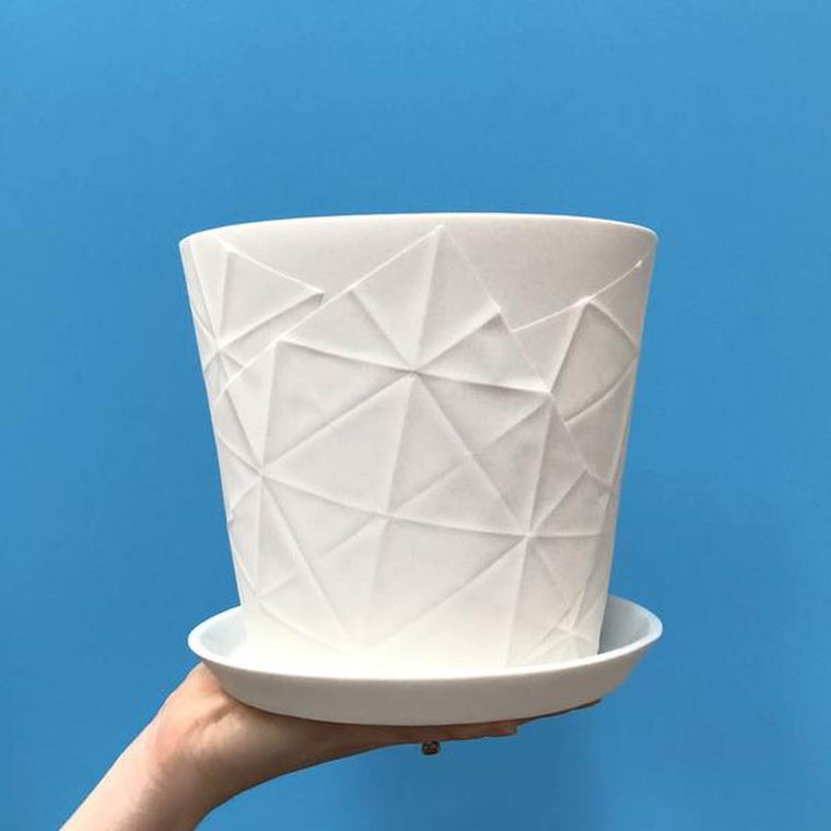 White porcelain planter with the imprinted creases from an unfolded chatterbox paper and a white dish held up by a hand against a blue wall. 