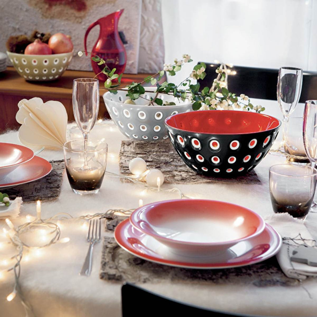 A table decorated and set with dinner plates in shades of red, black and white that tie in with the black & red Guzzini bowl in the centre. 