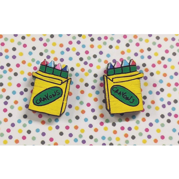 A pair of intricately hand coloured studs depicting packs of rainbow crayons. The packs are yellow with the word crayon written on them. Shown on a rainbow polka dot background.