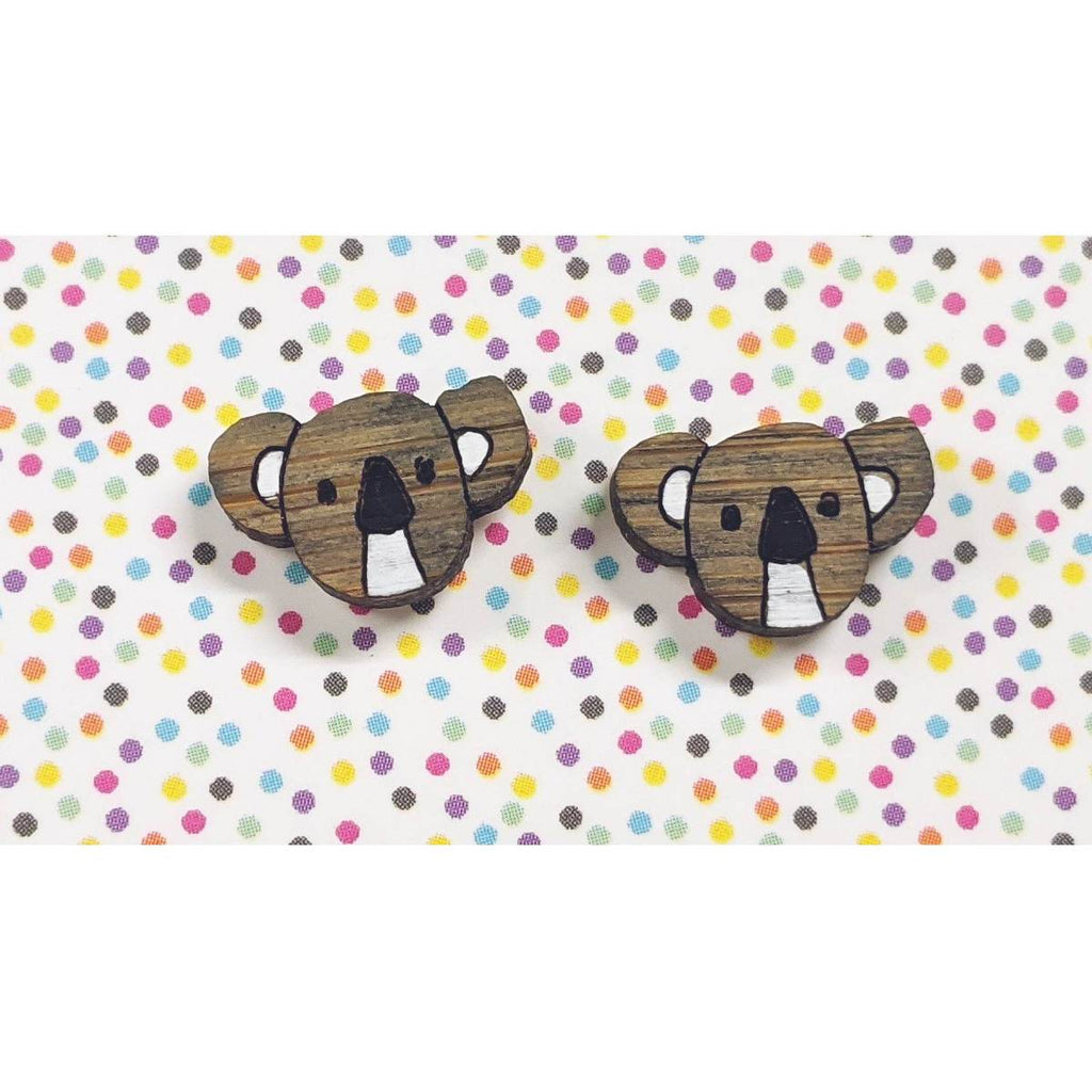 A pair of intricately hand coloured studs depicting koala heads, in grey and white. Displayed on a rainbow polka dot background.